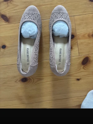 Beige ballerinaskor från Gyllene Gripen - Snygga beige ballerinaskor från Gyllene Gripen i mockaimitation med dekorativa utskurna mönster. Rundad tå och låg klack ger en klassisk look. Perfekta för dig som gillar stilrena och bekväma skor.