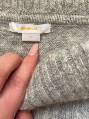 Ljusgrå off shoulder stickad tröja - Mysig ljusgrå stickad tröja från Gina Tricot med bred off shoulder-krage och långa ärmar. Tröjan har ribbstickade muddar vid ärmslut och nederkant, perfekt för att hålla värmen under kyliga dagar.