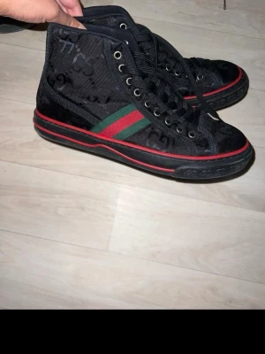 Svarta Gucci high top sneakers - Äkta Gucci skor, ni kan även skicka den till verifieringscentralen innan ni får den postad till er. Svarta high top sneakers från Gucci med klassiska gröna och röda ränder på sidan. Skorna har GG-monogram i tyget, svarta skosnören och röda detaljer längs sulan. Materialet är en mix av canvas och mocka för en lyxig känsla. Skorna går för cirka 8500 på affär. Pris kan diskuteras så tveka inte på att höra av er