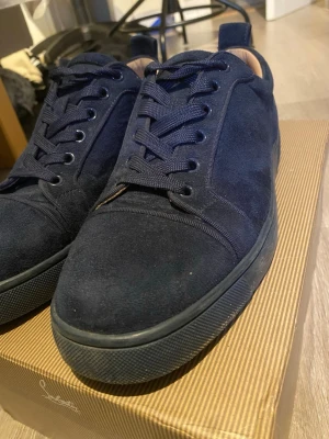 Mörkblå sneakers i mocka från Louboutin - Snygga mörkblå sneakers från Christian Louboutin i mjuk mocka med matchande mörkblå snörning och sula. Låg modell med diskret logga på hälen och ljus insida i läder. Perfekta för dig som gillar stilrena och exklusiva sneakers. Kan tvätta innan om det skulle behövas! Kan gå ner i pris