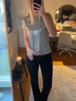 Silverig glittrig t-shirt - Snygg t-shirt med glittrig finish och korta ärmar. Perfekt för att lyfta en enkel outfit med lite extra shine. Rak passform och rund halsringning. Passar dig som gillar en stilren men ändå trendig look. Den är sjukt snygg i verkligheten, lite svårt att fånga på kamera!