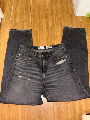 Gråa raka jeans - asos - Säljer ett par gråa jeans från Cropp med raka ben och slitna detaljer framtill. Jeansen har klassisk femficksdesign, synliga sömmar och en brun patch bak i midjan. Perfekta för en avslappnad streetstil.