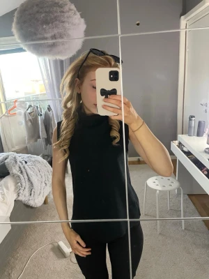Svart ärmlös topp från Zara - Snygg svart ärmlös topp från Zara med hög hals. Perfekt att styla med jeans eller kjol för en clean look. Mjuk och stretchig kvalitet som sitter skönt på kroppen. Enkel och stilren design som passar till många outfits.