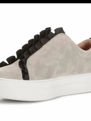 Grå  sneakers med svart volang  - Snygga beige sneakers från k cobler med cool svart volangdetalj på ovansidan. Skorna har en chunky vit sula och är tillverkade i mocka för en lyxig känsla. Perfekt för dig som vill sticka ut med din stil. St 38, men jag tycker är stora 38 passar bättre någon med st 39, jag säljer för  jag upplever dem är stora 