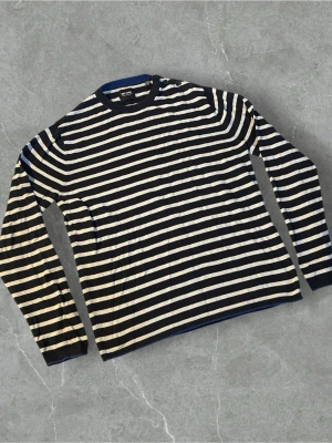 Randig stickad tröja Only & Sons | L - Snygg stickad tröja från Only & Sons med marinblå och vita horisontella ränder. Tröjan har rund halsringning med ribbad kant och två dekorativa knappar på axeln. Långärmad och i mjukt material, perfekt för en avslappnad stil.