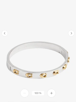 Coach armband i silver och guld - Snyggt armband från Coach i blankt silverfärgat metall med guldfärgade detaljer i form av små C-loggor runt om. Stilren och modern design som passar perfekt för att lyfta din outfit med en exklusiv touch.