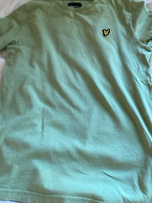 Grön t-shirt från Lyle & Scott - Snygg ljusgrön t-shirt från Lyle & Scott med klassisk passform och korta ärmar. T-shirten har en broderad gul logga på bröstet och är tillverkad i mjuk bomull. Perfekt för en avslappnad och stilren look.