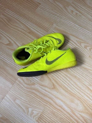 Nike gula fotbollsskor inomhus - Säljer ett par grymma gröna Nike fotbollsskor för inomhusbruk. Skorna har en låg profil, svart Nike-logga på sidan och svart detalj på sulan. Ovandelen är i mesh-liknande material för bra ventilation och passform. Perfekta för snabba vändningar på planen.