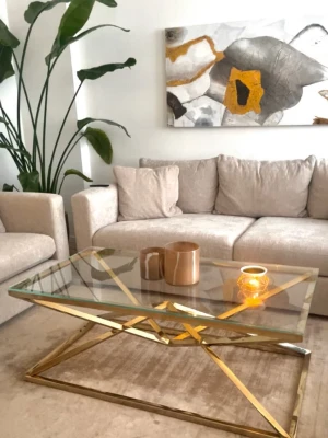 Elegant möbelpaket säljes - Stilrent soffbord med rektangulär glasskiva och modern guldfärgad metallram. Bordet har en unik geometrisk design på underredet och passar perfekt som mittpunkt i vardagsrummet. Bordsskivan är genomskinlig och ramen har en blank finish som ger en lyxig känsla.