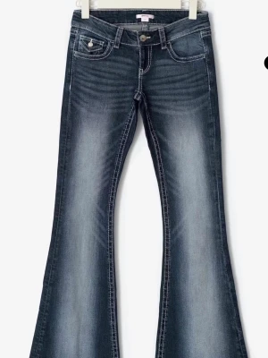 Mörkblå Jeans - Snygga mörkblå bootcut jeans med slitningar och markerade sömmar. Jeansen har broderade bakfickor med lock och knapp, samt klassisk femficksdesign. .
