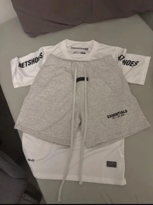 Grå Essentials shorts med snörning - Snygga grå shorts från Essentials med långa snören i midjan och tryckt logga på vänster ben. Modellen är loose fit och tillverkad i mjuk bomull, perfekta för en avslappnad stil. Passar dig som gillar streetwear och enkel design.