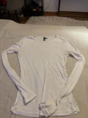 Vit genomskinlig ribbad långärmad topp - En enkel och stilren vit genomskinlig långärmad topp med ribbad struktur. Toppen har rund halsringning och är figurnära i modellen, perfekt att matcha med jeans eller kjol. Materialet känns mjukt och stretchigt.