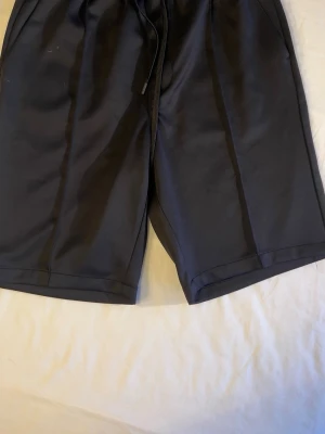 Svarta shorts med snörning - Svarta shorts med avslappnad passform och snörning i midjan. De har fickor på sidorna och en bakficka. Perfekta för sommaren och tillverkade i ett mjukt material som känns skönt mot huden.