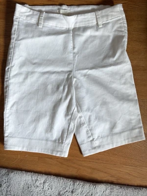 Vita shorts från H&M i bomull - Snygga vita shorts från H&M i storlek 34. Klassisk modell med hällor för bälte och raka ben. Tillverkade i bomull, perfekta för varma dagar. Enkla att matcha med olika toppar för en fräsch look.