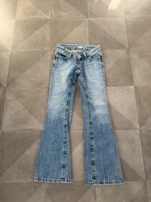 Ljusblå bootcut jeans från Gina tricot  - Snygga ljusblå bootcut jeans från Gina tricot med klassisk femficksdesign och låg midja. Jeansen har slitningar och en lätt tvättad look, perfekta för en avslappnad stil. Tillverkade i bomullsdenim med dragkedjegylf.