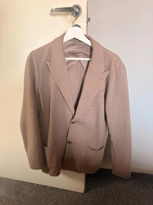 Beige John henric Blazer - Stilren beige kavaj från John Henric i 100% bomull. Klassisk modell med breda slag, tre utanpåfickor och en bröstficka. Perfekt för en dressad look med en modern touch. Fodrad insida för extra komfort. Erbjudandet gäller fram till onsdag 23.59, nypris på 1499 kronor