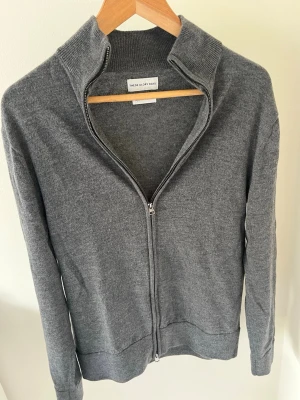 Grå fullzip merinoulltröja  - Snygg grå tröja från These Glory Days i mjuk superior merinoull. Tröjan har hel dragkedja framtill, hög krage och ribbade muddar. Perfekt för lager-på-lager och enkel att matcha med jeans eller chinos. Tröjan har en liten lagning som knappt syns (bild 5). Storlek M kan passa S.