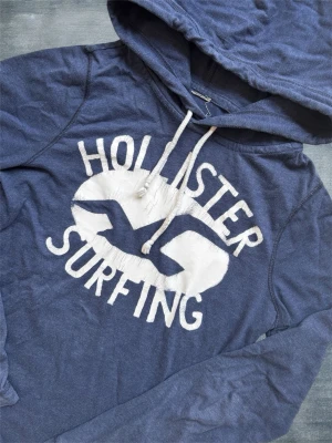 Hollister Hoodie med Tryck - En mycket trevlig hoodie från Hollister i ett lite tunnare material vilket gör den perfekt till vår/sommar! Sitter som S/M, modellen är 178 cm och väger 68 kg. Hör av dig vid frågor! 