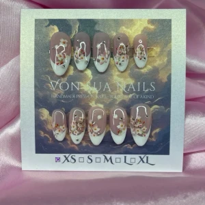 SoftSakura (XS);Medium Almond - Handgjorda press-on naglar i en medium mandelform med fransk tipp. Basen är nude/rosa och tipparna är vita, dekorerade med små-blommor, pärlor och silverdetaljer. Perfekt för dig som vill ha unika och detaljerade naglar med lyxig känsla.