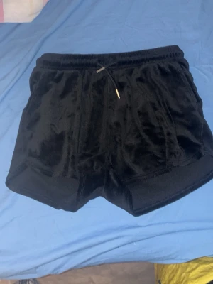 Svarta velourshorts med snörning - Svarta shorts i mjuk velour med elastisk midja och snörning framtill. Klassisk sportig modell med fickor på sidorna och en bakficka. Perfekta för en avslappnad och chill stil.