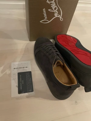 Två par sneakers från Christian Louboutin - Snygga svarta sneakers från Christian Louboutin med klassisk röd sula och diskret logga. Skorna har en låg profil, rund tå och är tillverkade i mocka med läderdetaljer. Perfekta för dig som vill ha en exklusiv och stilren look.