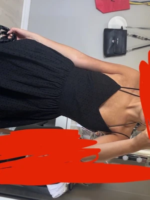 Svart kort klänning med tunna band - Säljer en svart kort klänning med tunna axelband och v-ringning. Klänningen har ett diskret prickigt mönster och är lätt utställd i kjolen. Perfekt för varma dagar och enkel att styla med accessoarer.