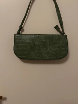 Grön axelväska  - Snygg grön handväska med axelrem i krokopräglat konstläder. Väskan har en avlång, rektangulär form och minimalistisk design. Perfekt för dig som gillar trendiga accessoarer med lite edge 💕