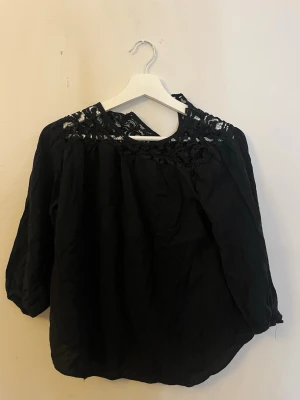 Svart blus med spetsdetaljer - Svart blus med trekvartsärm och fina spetsdetaljer vid axlar och halsringning. Blusen har en lös passform!                                                              Snyggare skick när den är struken:)