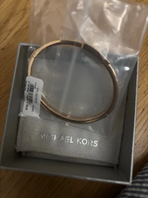 Roséguldigt armband Michael Kors - Snyggt och stilrent armband från Michael Kors i roséguldfärgad rostfritt stål. Armbandet har en enkel och elegant design som passar perfekt till alla outfits. Levereras i originalask med Michael Kors-logga.