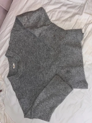 Grå stickad tröja  - Mysig grå stickad tröja med rund hals och breda ribbade muddar vid ärmslut och nederkant. Tröjan har en avslappnad passform och är tillverkad i en mjuk ullblandning som känns skön mot huden. Perfekt för kyliga dagar.