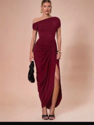 Vinröd offshoulder långklänning - Snygg vinröd långklänning med offshoulder-design och draperad detalj i sidan. Klänningen har en hög slits och figurnära passform som framhäver siluetten. Perfekt för dig som vill sticka ut med en elegant look.