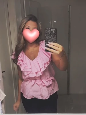 Rosa volangblus med omlottkänsla - Söt rosa blus med volangdetaljer och v-ringning. Toppen har omlottkänsla och knyts i midjan för en feminin siluett. Perfekt för dig som gillar romantisk stil.