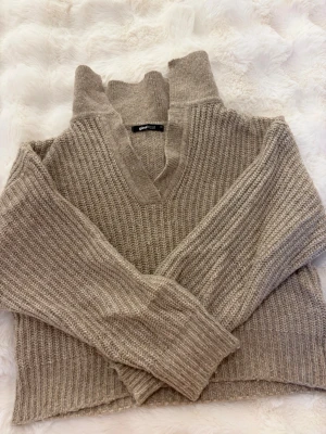 Beige stickad tröja från Gina Tricot - Beige stickad tröja från Gina Tricot med v-ringning och krage. Tröjan har grovstickad struktur, långa ärmar och ribbade muddar. Perfekt för lager-på-lager och en chill look.