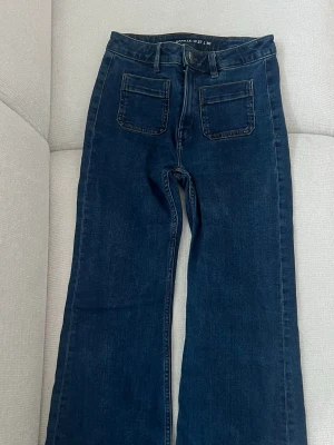 Mörkblå jeans Camille W27 L30 - Snygga mörkblå jeans med raka ben och hög midja. Jeansen har två stora framfickor och bälteshällor. Tillverkade i klassisk denim med en stilren look som passar till det mesta.