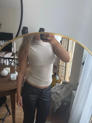 Beige ärmlös topp från Zara - Säljer en stilren beige ärmlös topp från Zara. Toppen har en hög halsringning och är figurnära i modellen, vilket ger en snygg och modern look. Tillverkad i mjuk bomullsmix som känns skön mot huden. Perfekt att matcha med både jeans och kjol.