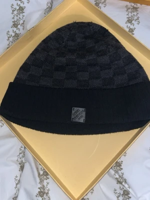 Svart Louis Vuitton mössa med rutmönster ÄKTA - Säljer en svart mössa från Louis Vuitton med klassiskt diskret rutmönster och vikt kant. Mössan har en liten patch med Louis Vuitton-loggan framtill. Perfekt accessoar för dig som vill ha en stilren och exklusiv look. ÄKTA ANVÄND I RUNT TVÅ VECKOR KARTONG MEDFÖLJER!