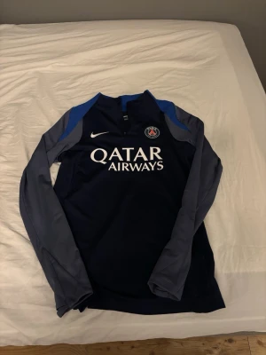 PSG Nike träningströja blå - Säljer en snygg Paris Saint-Germain träningströja från Nike i marinblått med gråa ärmar och blå detaljer vid axlarna. Jag kan även göra byten.