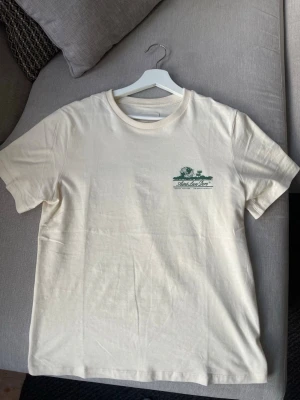 Aimé Leon Doré T-shirt – off white – strl S - T-shirt från Aimé Leon Doré med liten bröstprint och stor ryggprint. Väldigt eftertraktad modell från ALD och svår att få tag på i Sverige.  Ren och tidlös design som passar till jeans, chinos eller shorts.  Öppen för bud! Skick: Mycket bra Storlek: S Färg: Off white med grön print  Nypris ca 1299+ kr. Pris: 399  kr