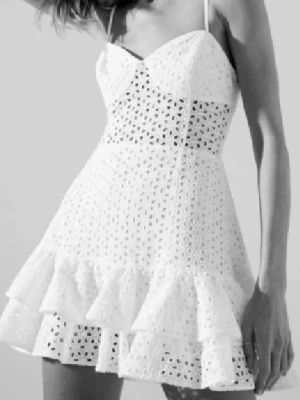 Vit kort klänning med volang - Supersöt vit kort klänning från zara, Denna klänning finns inte att köpa längre. Den har tunna axelband och ett av axelbanden råka jag klippa av när jag öppnade paketet men jag sydde ihop de och de syns ej och det är ingen fara att de ska gå sönder då jag använt den här klänningen och den har suttit ihop utan något problem. Klänningen har broderade hål och volangkant nertill och markerad midja med genombrutet mönster. Perfekt för sommarens alla tillfällen och ger en fräsch och romantisk vibe.