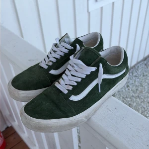 Gröna Vans Old Skool sneakers - Mörkgröna Vans Old Skool sneakers i mocka med klassisk vit sidostripe och vita skosnören. Yttersulan är vit och har den typiska Vans-looken. Perfekta för dig som gillar streetwear och vill ha en tidlös stil.