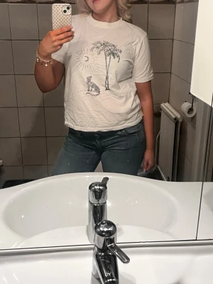 Vit t-shirt med palm och leopard - Vit t-shirt med tryck av en palm, sol och leopard på framsidan. Klassisk rund hals och korta ärmar. Skön och avslappnad passform, perfekt till jeans eller shorts. Materialet känns mjukt och bekvämt mot huden.