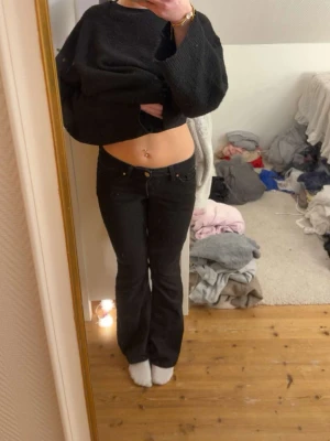 Svarta bootcut jeans med låg midja - Säljer ett par svarta bootcut jeans med låg midja och klassisk femficksdesign. Jeansen har en smal passform upptill och lätt utsvängda ben. Perfekta till en avslappnad och trendig look. Materialet ser ut att vara denim med stretch.