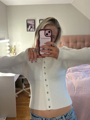 Vit ribbstickad kofta med knappar - Snygg vit ribbstickad kofta med silvriga knappar framtill + är figurnära i modellen💞