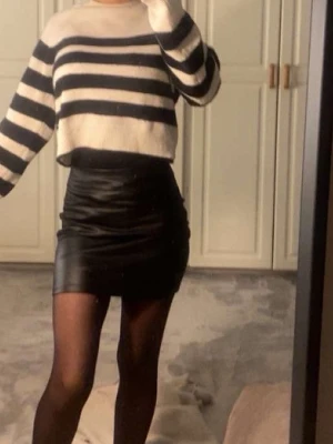 Svart tight minikjol i skinnimitation - Säljer en svart tight minikjol i skinnimitation. Kjolen har en kroppsnära passform och en kort längd som ger en trendig look. Perfekt att styla med stickad tröja eller crop top för en cool outfit.