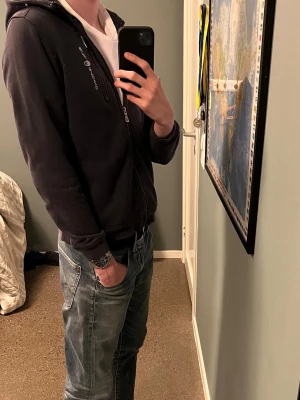 Svart/blå zip hoodie från sail racing - Säljer en svart/blå hoodie med dragkedja från Sail racing. Hoodien har en klassisk passform, fickor fram och logga på bröstet. Hoodiens orginal pris är 1000kr och har inte använt den så mycket men har ändå lite små tecken på att den är användbar fast enbart ifall man kollar noga