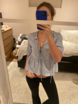 Ljusblå volangblus med knyt från H&M - Söt ljusblå blus från H&M med volang nedtill och knytning framtill. 