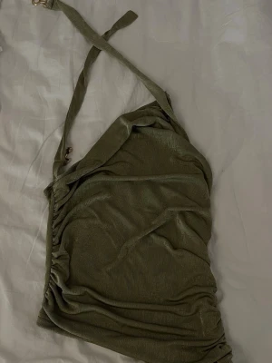 Olivgrön oneshoulder topp - Trendig olivgrön topp med oneshoulder-design och smala axelband. Toppen har en lätt rynkad effekt på sidan och är tillverkad i ett mjukt, stretchigt material som ger en snygg passform. Perfekt för dig som vill sticka ut med en unik och modern look.