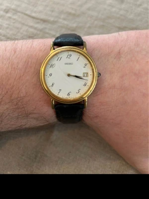 90-tals Seiko Guldpläterad 36mm Vintage - Säljer en snygg vintage klocka från eftertraktade japanska Seiko i gott men använt skick. Finns repor och skavanker medan plasten är kvar på baksidan (ej smuts). Går bra, läderarmband, datumvisare, vattentät, osv. Behöver nytt batteri. Fås i klocklåda.  Begagnat pris: 900+ SEK Mitt pris: 598 SEK  Skickas spårbart samma dag mot eller hämtas i Glumslöv.  Hör av dig vid frågor och se gärna mina andra annonser också!