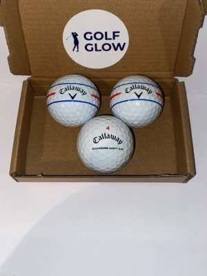 Callaway Chromesoft tripple track 3-pack  - Tre vita Callaway Chrome Soft X golfbollar med röda och blå linjer, levereras i en enkel brun kartong med GOLF GLOW-klistermärke. Perfekta för dig som vill ha kvalitetsbollar till golfbanan.