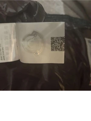 Svart dunjacka från Moncler - Snygg svart dunjacka från Moncler med glansig finish och klassisk Moncler-logga på insidan. Jackan har en modern look och är tillverkad i slitstarkt material med dunfyllning som håller dig varm under kalla dagar.